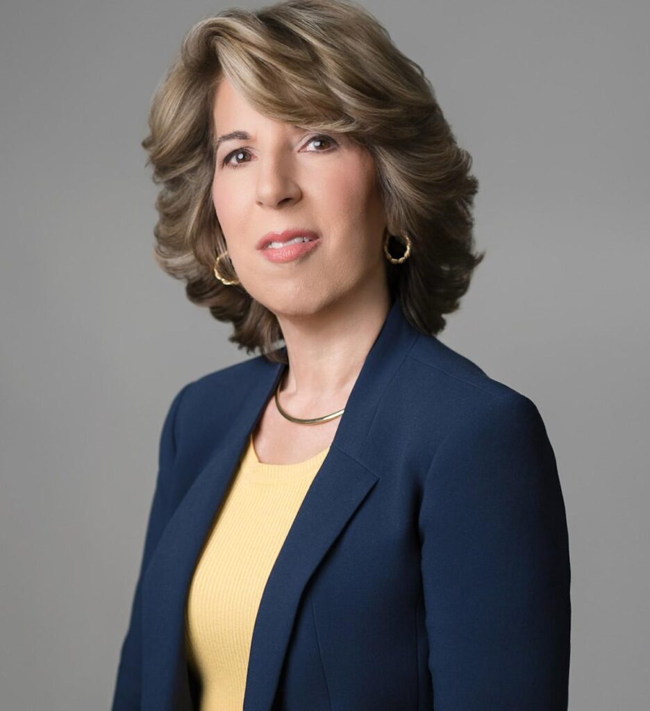 Professional corporate headshot of a woman wearing a navy blazer and yellow blouse in a studio