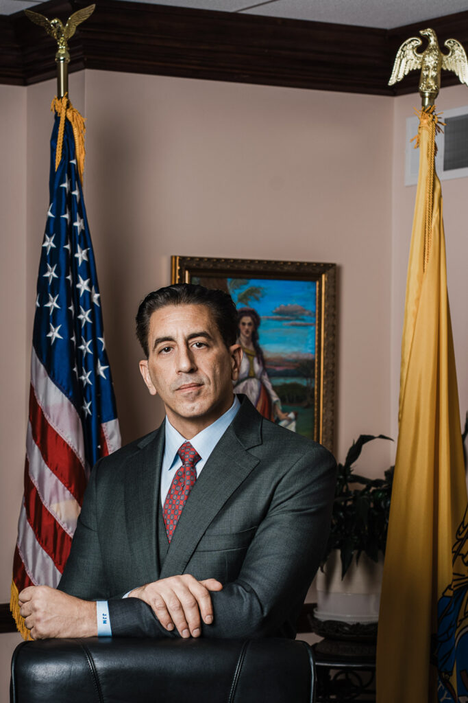 Authentic business headshot of an attorney photographed in his Bergen County NJ office between the American and New Jersey state flags.