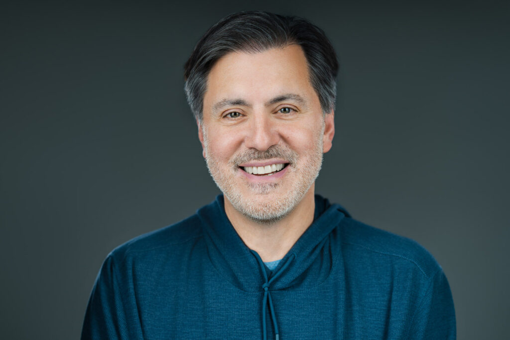 Barry actor headshot in blue hoodie with warm natural smile against gray background