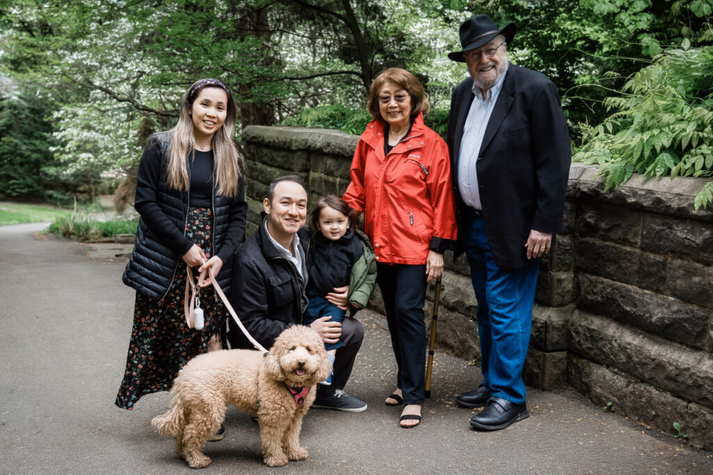 Candid family photography session by stone wall path in Tenafly NJ with three generations and dog 