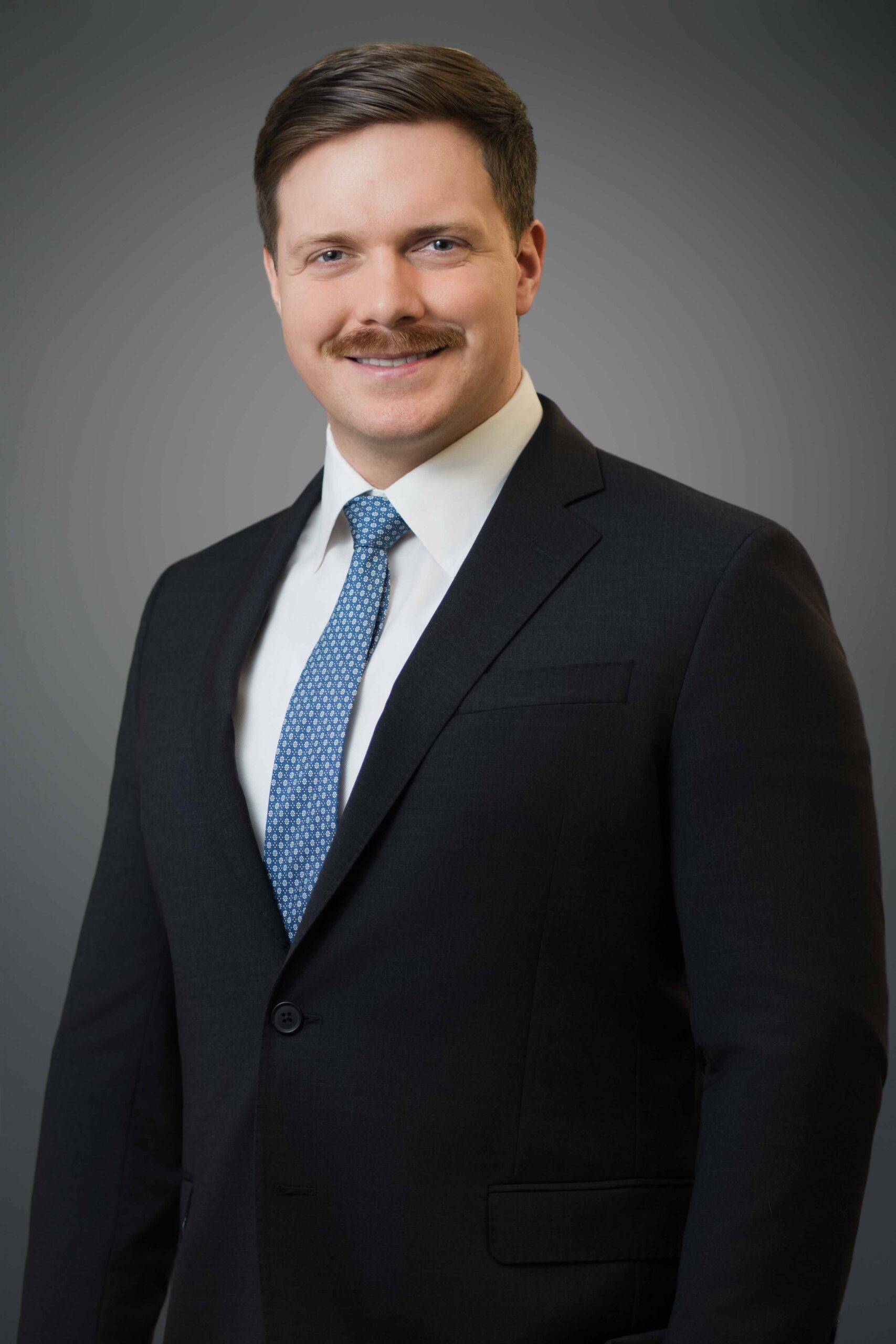 Professional executive headshot in NYC with confident and approachable expression against neutral gray background