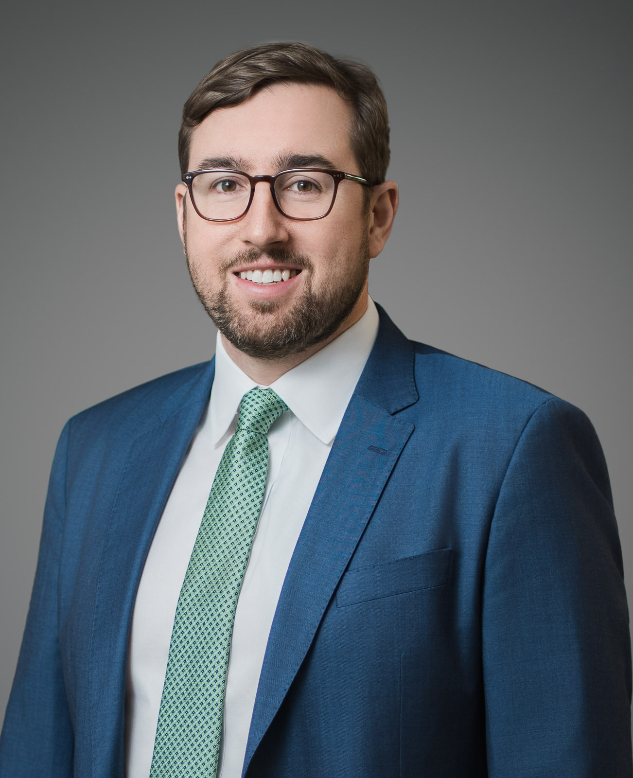Man in glasses and blue suit smiling in a professional corporate headshot