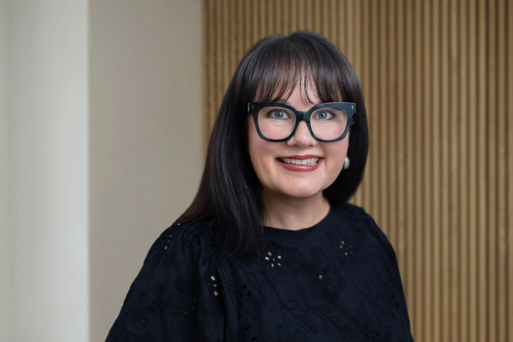 Professional executive headshot NYC, woman with dark hair and green glasses, warm natural smile
