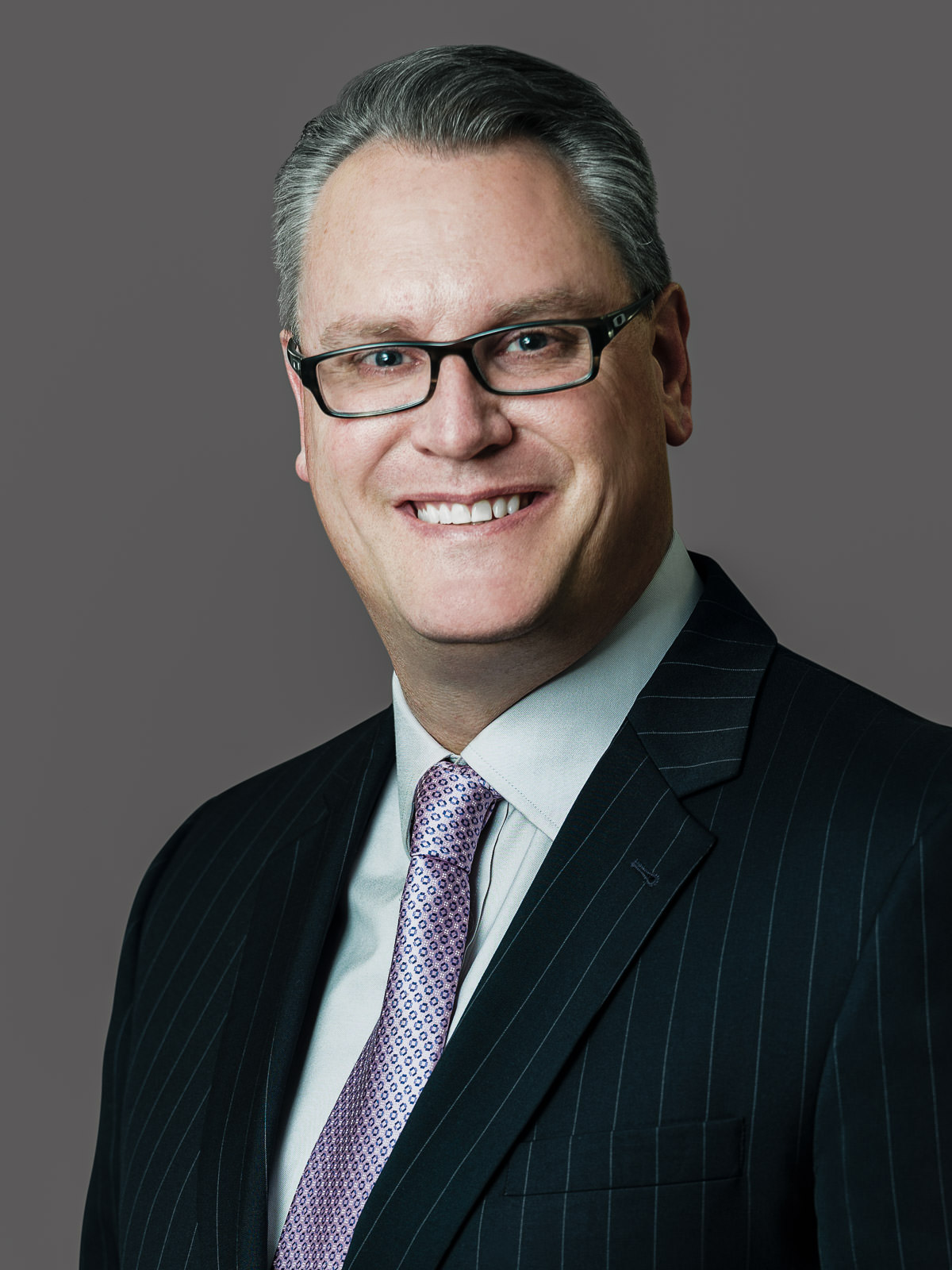 Senior executive in navy pinstripe suit during a professional headshot session on grey studio backdrop