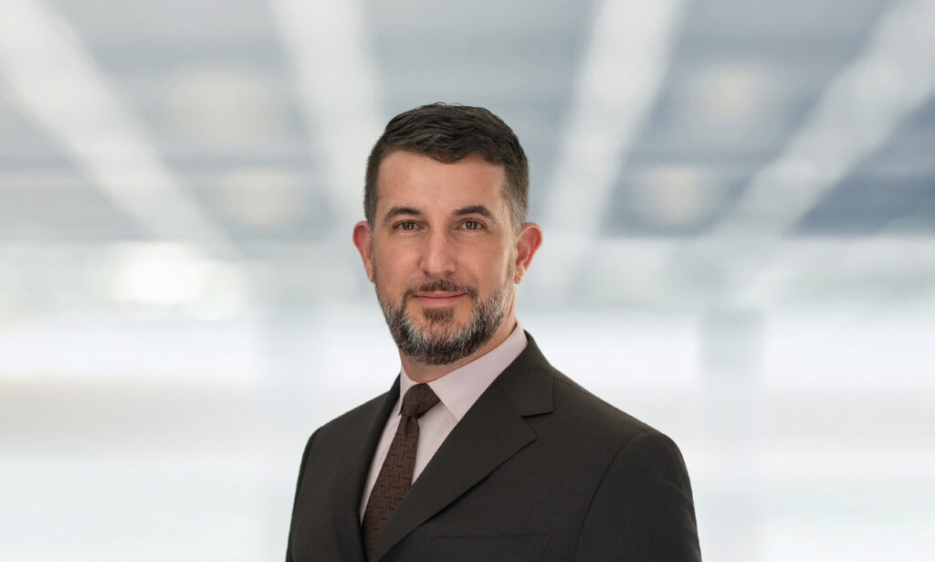 Adam Birnbaum in a dark suit against a softly blurred corporate-style background