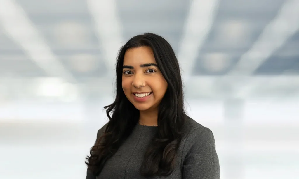 Professional headshot of a smiling woman in charcoal business attire against a softly blurred background