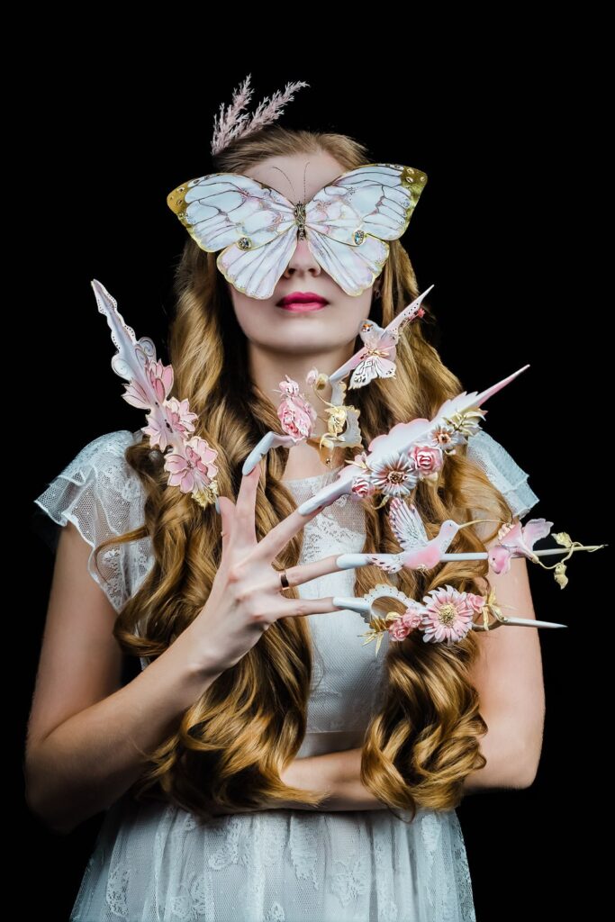 Model wearing a butterfly mask displaying sculpted nail art in our New Milford NJ studio