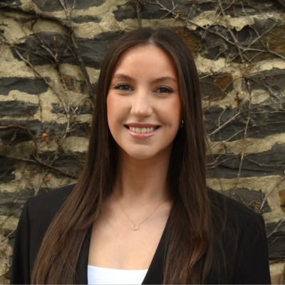 Professional poses in black blazer for business casual headshot near stone wall in Northern New Jersey