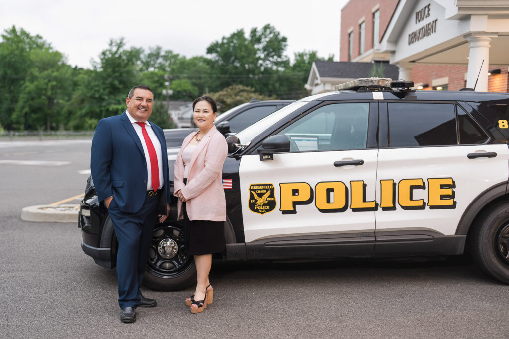 Two candidates standing beside a Ridgefield police vehicle outside the police department in New Jersey