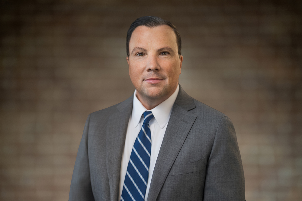 Executive in a charcoal suit photographed against a softly blurred corporate background