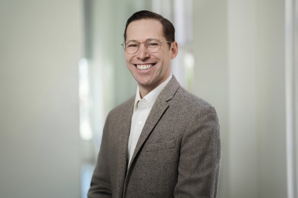 Architect in herringbone blazer smiling during environmental LinkedIn headshot session in office daylight