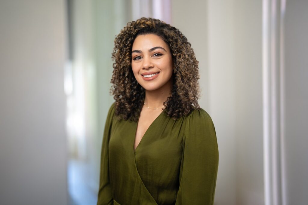 Smiling employee in olive wrap top photographed for company headshots in a softly lit office