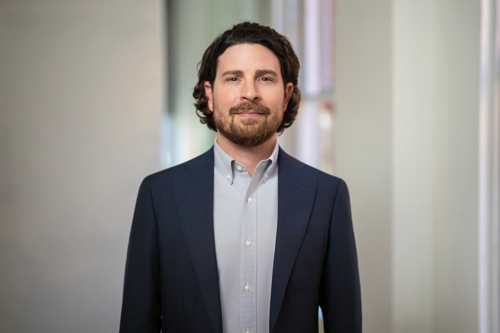 Corporate team member in navy blazer photographed for a corporate headshot in a sunlit office hallway