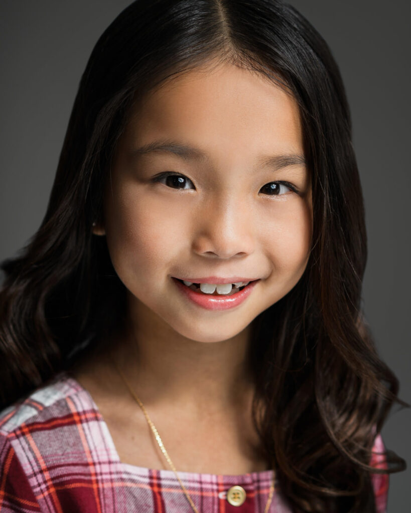 Child actor smiling in her own plaid top during a New Milford NJ headshot session