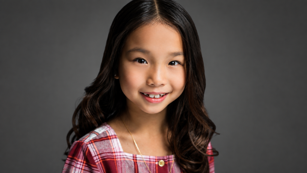 Child actor smiling in her own plaid top during a New Milford NJ headshot session
