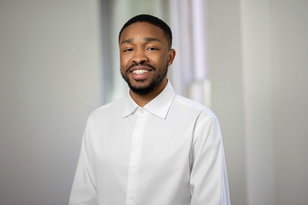 Smiling employee in white dress shirt photographed under matching headshot lighting in a bright office