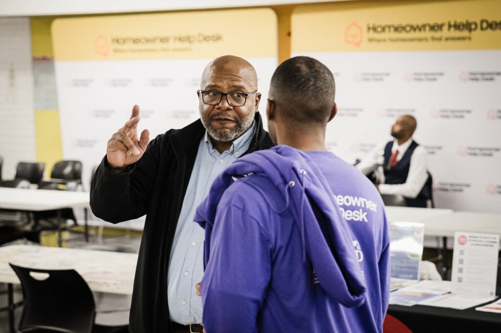 Community outreach event participants talking in front of the Homeowner Help Desk backdrop at Bronx House