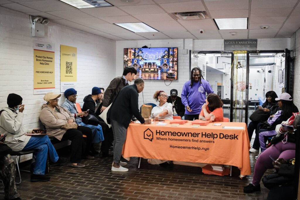 People seated near the Homeowner Help Desk table during the Bronx Homeowner Help Clinic