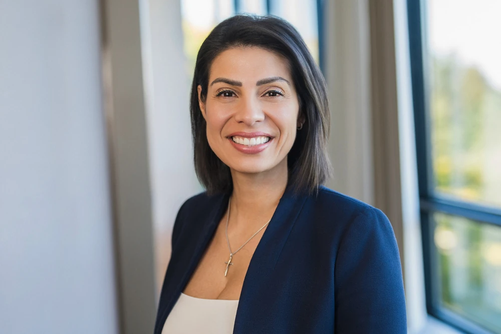 Smiling financial advisor in a navy blazer photographed indoors beside office windows