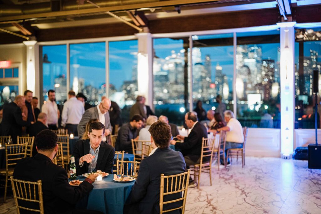 Guests dining at the evening reception at Liberty House with the Manhattan skyline lit up behind them